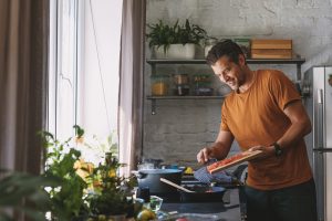 Jeune homme heureux beau mettant les légumes coupés à une poêle